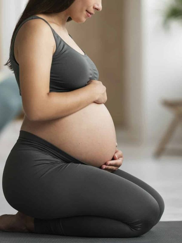 Young Pregnant Woman Embracing Belly While Sitting On Yoga Mat At Home